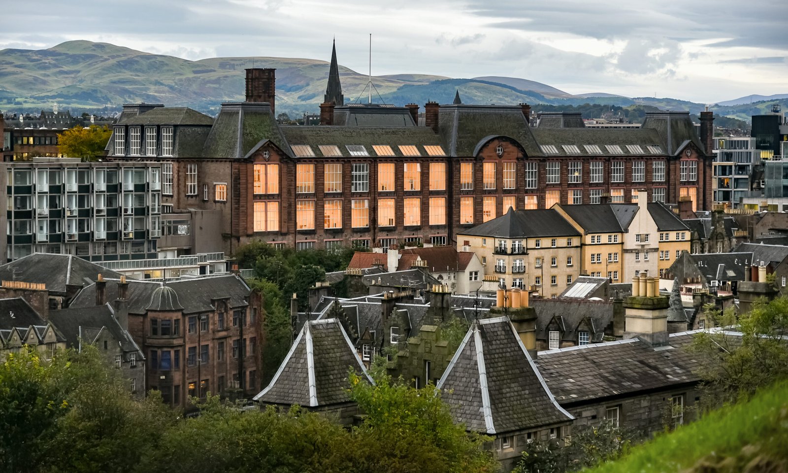 Alt text: View of the University of Edinburgh architecture at dusk, with the Hills in the background.