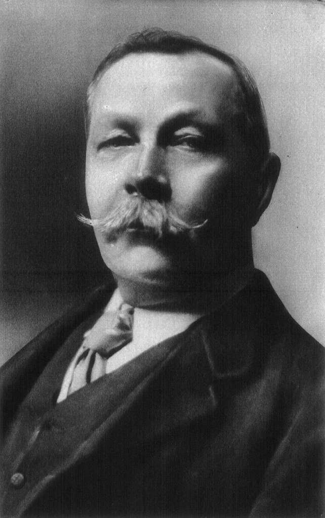 Black and white portrait of Sir Arthur Conan Doyle in 1914, wearing a formal suit and seated with a composed expression.